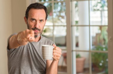 Orta yaş erkek içme kahve bir fincan kamera ve size parmak ile işaret, el işareti, pozitif ve kendinden emin bir jest ön