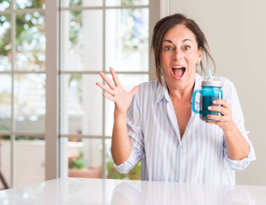 Orta yaşlı kadın içme milkshake bir cam çok mutlu ve heyecanlı, kocaman bir gülümseme ile çığlık ve ellerini kaldırdı kazanan ifade kutluyor zafer