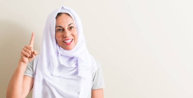 Gülen yüz, bir numara ile bir fikir ya da soru işaret parmağı ile orta yaş Arap kadın beyaz hijab giyen şaşırttı