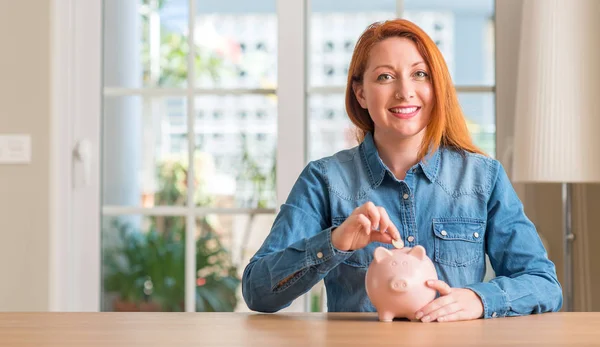 Pelirroja Mujer Ahorra Dinero Alcancía Casa Con Una Cara Feliz — Foto de Stock