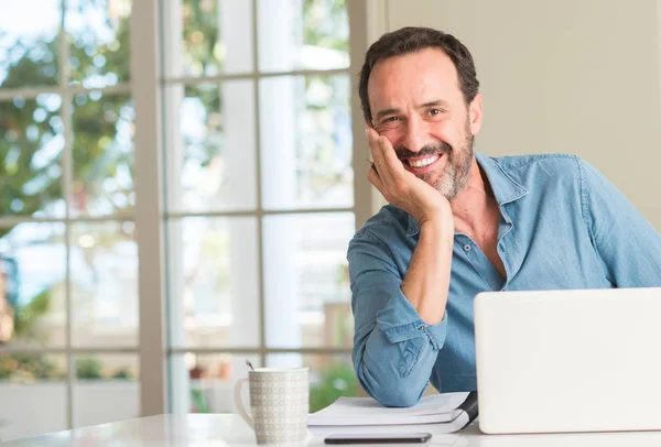 Middle age man using laptop at home with a happy face standing and smiling with a confident smile showing teeth