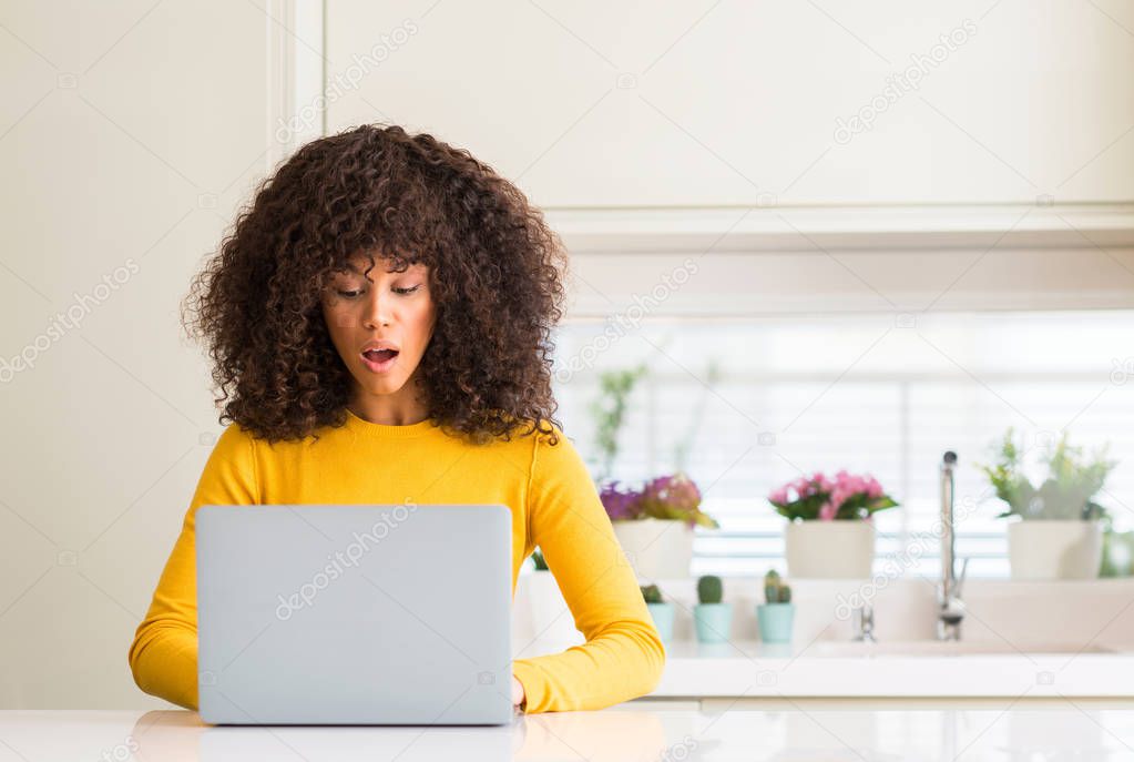 African american woman using computer laptop at kitchen scared in shock with a surprise face, afraid and excited with fear expression