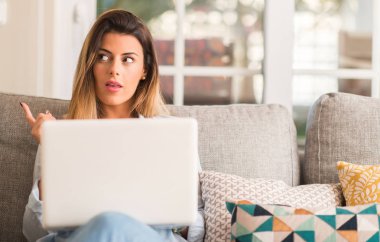 Genç güzel kadın kanepe düşünme üzerinde dizüstü bilgisayar kullanarak bir fikir.