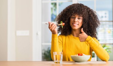 Afrikalı-Amerikalı kadın yemek makarna salatası, ok işareti yapıyor büyük gülümseme ile mutlu ev, parmaklarıyla, mükemmel işaret parmak