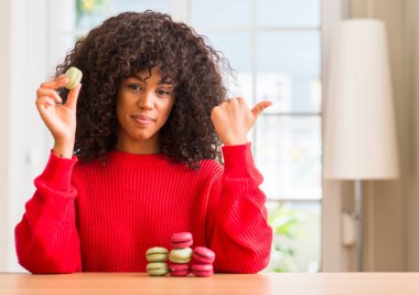 El ve parmak ile mutlu yüz gülümseyen ile yukarıyı macaron tutan Afrikalı-Amerikalı kadın