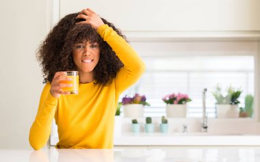 Afrikalı-Amerikalı kadın elle kafasına, stresli bir bardak portakal suyu içme şok utanç ve sürpriz suratla, öfkeli ve sinirli. Korku ve hata için üzgün.