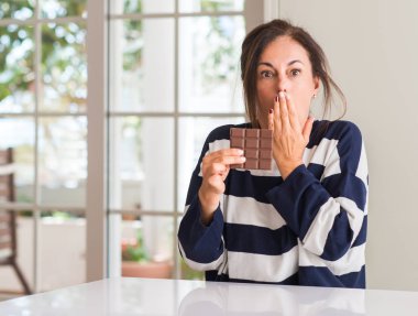 Orta yaşlı kadın yeme çikolata bar kapak ağız el için hata, ifade korku, utanç ile şok ile sessizlik içinde gizli kavramı korkuttu