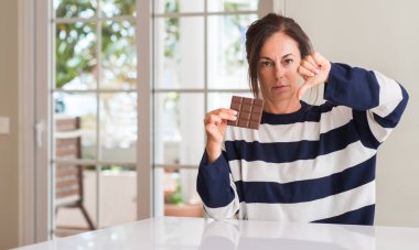 Kızgın yüz, eksi işareti aşağı antipati başparmak ile gösterilen, ret kavramı ile çikolata yeme orta yaşlı kadın