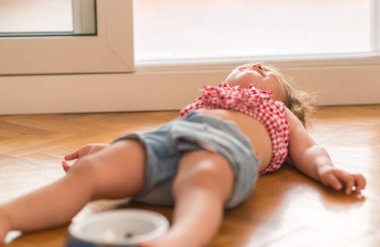 Beautiful blond child crying and shouting with tantrum laying on the floor at home. clipart