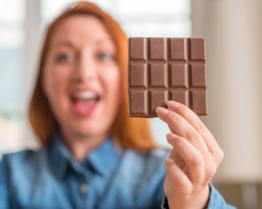 Kocaman bir gülümseme ile çığlık zaferini kutluyor ve ellerini kaldırdı evde çok mutlu ve heyecanlı, kazanan ifade çikolata tutan Kızıl saçlı kadın