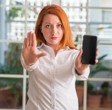 Açık eliyle dur işareti ile ciddi ve kendine güvenen ifade, savunma jest yapıyor evde Smartphone kullanan Kızıl saçlı kadın