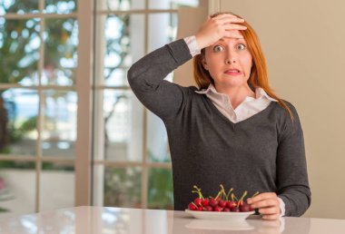 Kızıl saçlı kadın yemek utanç ve sürpriz yüz ile şok baş, el ile evde kiraz vurguladı öfkeli ve sinirli. Korku ve hata için üzgün.