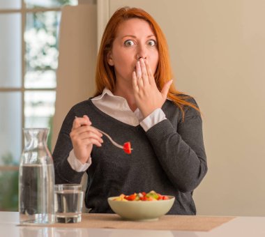 Kızıl saçlı kadın yeme meyve tabağı, kivi ve çilek evde ağız el hata, korku, sessizlik içinde gizli kavramı korkmuş ifade için utanç ile şok ile kapak