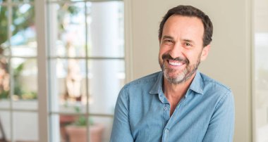 Yakışıklı orta yaş adam ayakta ve diş gösterilen kendine güvenen bir gülümsemeyle gülümseyerek mutlu bir yüz ile