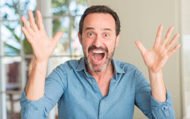 Yakışıklı orta yaş erkek çok mutlu ve heyecanlı, kazanan ifade büyük gülümseme ile çığlık ve ellerini kaldırdı zaferini kutluyor