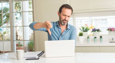 Dizüstü evde kullanan kızgın yüzü, eksi işareti aşağı antipati başparmak ile gösterilen, ret kavramı ile orta yaş adam