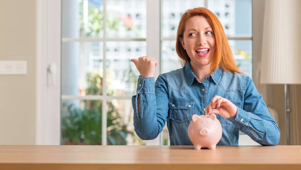 幸せそうな顔を笑顔で手と指指している赤毛の女性は 自宅の貯金箱でお金を節約 — ストック写真