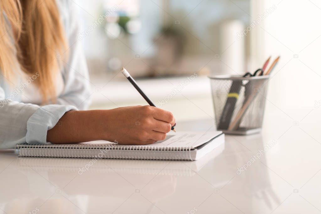 Young beautiful woman hands writting on a book while studying at home