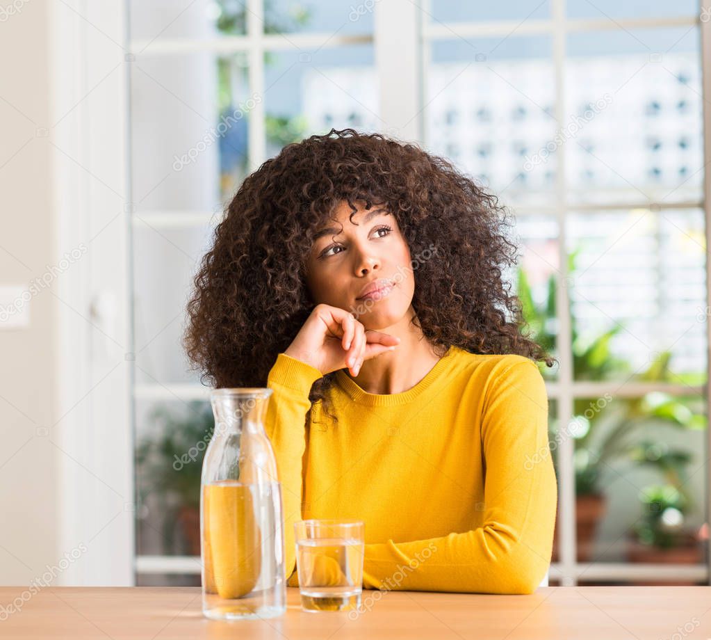 African american woman drinking a glass of water at home serious face thinking about question, very confused idea