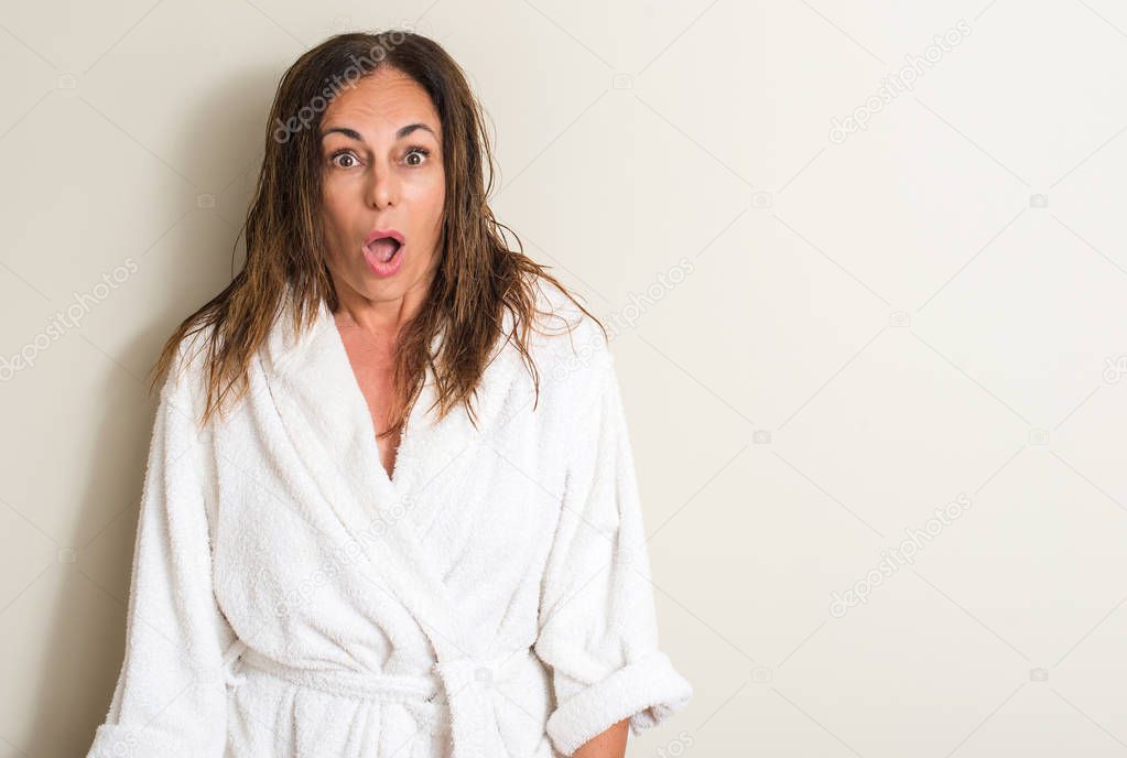 Beautiful middle age woman, wet hair wearing a towel scared in shock with a surprise face, afraid and excited with fear expression