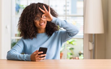 Mutlu yüz el parmaklarının arasından seyir göz üzerinde ok işaretiyle yapıyor gülümseyen ile Smartphone kullanarak güzel bir Afrikalı-Amerikalı kadın