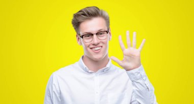 Gösterilen ve parmakları ile işaret genç yakışıklı sarışın adam kendinden emin ve mutlu gülümseyerek süre beş numara.