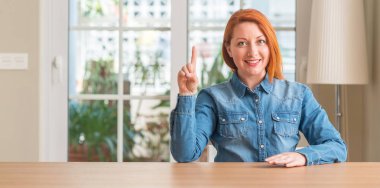 Kızıl saçlı kadın evde gösterilen ve kendinden emin ve mutlu gülümseyen bir parmak ile işaret eden oktan yukarı.