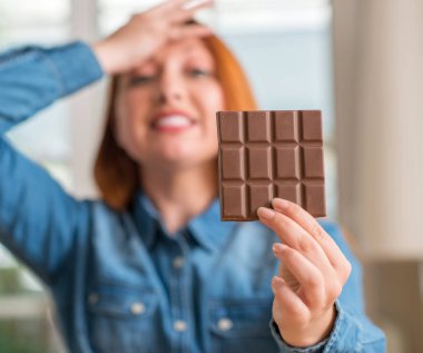 Baş, el ile vurguladı evde çikolata bar tutan Kızıl saçlı kadın şok utanç ve sürpriz suratla, öfkeli ve sinirli. Korku ve hata için üzgün.