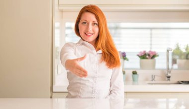 Kızıl saçlı kadın dostu sunan el sıkışma tebrik ve davet edici olarak gülümseyen mutfak at. Başarılı iş.