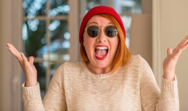 Yün şapka ve güneş gözlüğü çok mutlu ve heyecanlı, giymiş şık Kızıl saçlı kadın kazanan ifade büyük gülümseme ile çığlık ve ellerini kaldırdı zaferini kutluyor