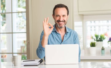 Dizüstü evde kullanan orta yaş adam parmak, mükemmel sembolü ile ok işareti yapıyor
