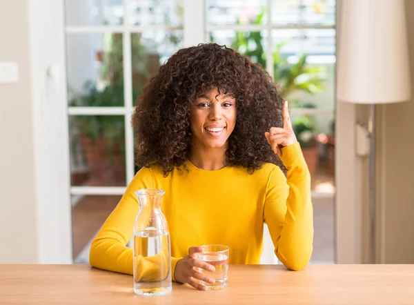 家庭での水のガラスを飲むアメリカ人のアフリカの女性のアイデアを驚かせたまたは幸せそうな顔で人差し指を質問 ナンバーワン — ストック写真