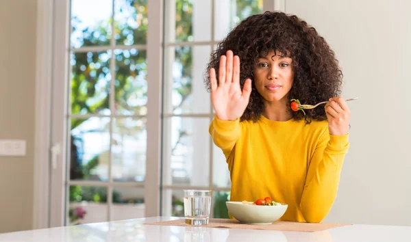 African american woman eating pasta salad with open hand doing stop sign with serious and confident expression, defense gesture