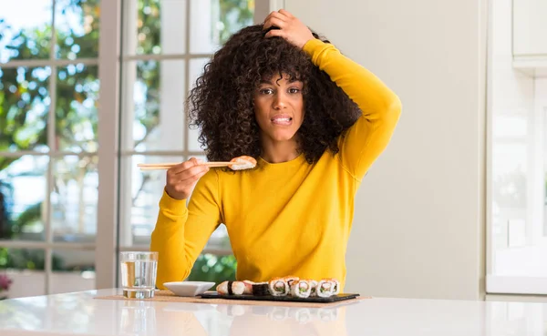 African american woman eating sushi using chopsticks at home stressed with hand on head, shocked with shame and surprise face, angry and frustrated. Fear and upset for mistake.