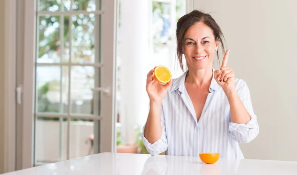 アイデアや質問 ナンバーワンの幸せそうな顔で指を指していると驚かれるオレンジ色の果物を保持している中年の女性 — ストック写真