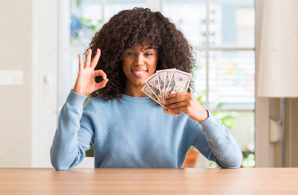 African american woman holding dollar bank notes doing ok sign with fingers, excellent symbol