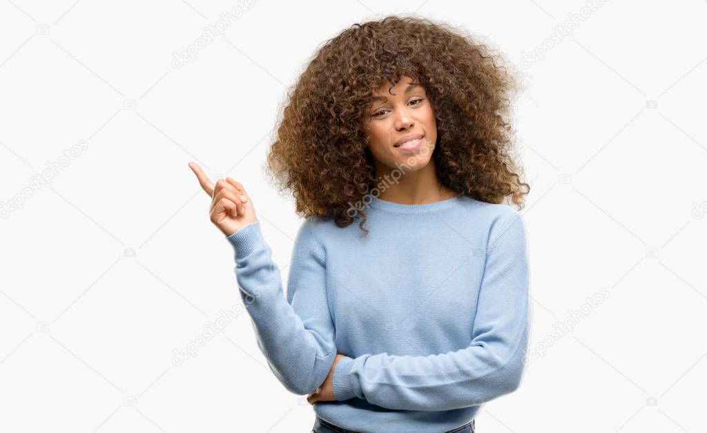 African american woman wearing a sweater with a big smile on face, pointing with hand and finger to the side looking at the camera.