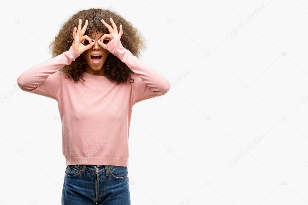 African american woman wearing pink sunglasses doing ok gesture like binoculars sticking tongue out, eyes looking through fingers. Crazy expression.