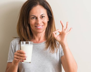 Bir bardak taze süt parmak, mükemmel sembolü ile ok işareti yapıyor içme orta yaş kadın