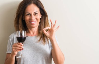 Orta yaş kadın parmakları, mükemmel sembolü olan ok işareti yapıyor bir bardak kırmızı şarap içme
