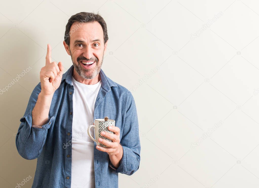 Senior man drinking coffee in a mug surprised with an idea or question pointing finger with happy face, number one