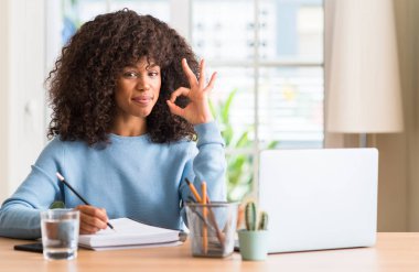 Afrikalı-Amerikalı kadın eğitimi evde parmak, mükemmel sembolü ile ok işareti yapıyor bir bilgisayar dizüstü kullanarak