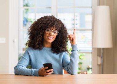 Bir fikir ya da soru işaret parmağı gülen yüz, bir numara ile Smartphone sürpriz kullanan güzel Afrikalı-Amerikalı kadın