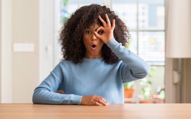 Afrikalı-Amerikalı kadın evde ok jest sürpriz yüz, göz parmaklarının arasından seyir şok yapıyor. İmansız ifade.