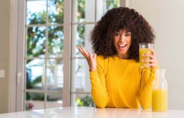 Sağlıklı meyve suyu evde çok mutlu ve heyecanlı, kocaman bir gülümseme ile çığlık zaferini kutluyor kazanan ifade içme ve ellerini kaldırdı Afrikalı-Amerikalı kadın