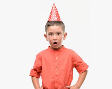 Koyu saçlı küçük çocuk Doğum günü şapkası korkuyor şok sürpriz yüz, korkuyor ve heyecanlı korku ifadesi ile