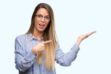 Güzel genç kadın şık gömlek ve hayrete ve el ile sunulması ve parmak ile işaret ederken kameraya gülümseyen gözlük.