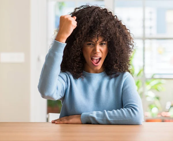 African american woman at home angry and mad raising fist frustrated and furious while shouting with anger. Rage and aggressive concept.