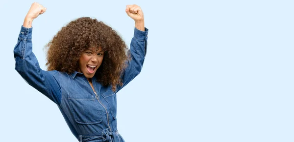 アフリカ系アメリカ人の女性は幸せと興奮の大成功 エネルギーおよび肯定的な感情を表現する勝利を祝って青いジャンプ スーツを身に着けています 新しい仕事の喜びを祝う — ストック写真
