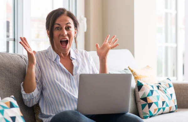 Kocaman bir gülümseme ile çığlık zaferini kutluyor ve ellerini kaldırdı kanepe çok mutlu ve heyecanlı, kazanan ifade içinde dizüstü bilgisayar kullanan kadın orta yaşlı